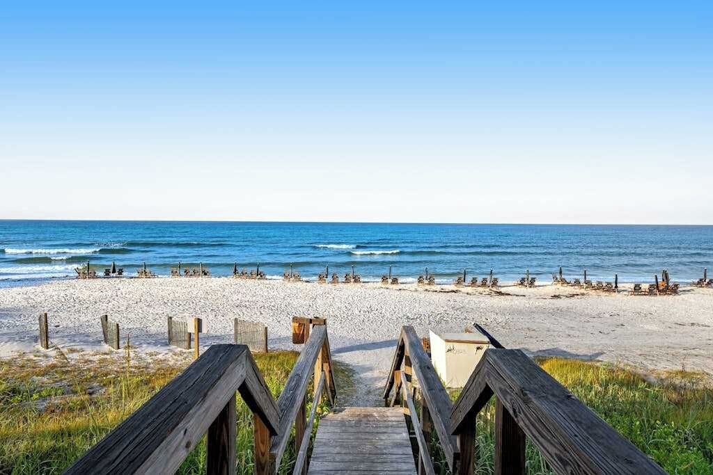 A wooden boardwalk leading to a beach with a clear sky.