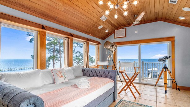 Een slaapkamer met een groot bed, uitzicht op zee, een balkon met een telescoop en een houten plafond.
