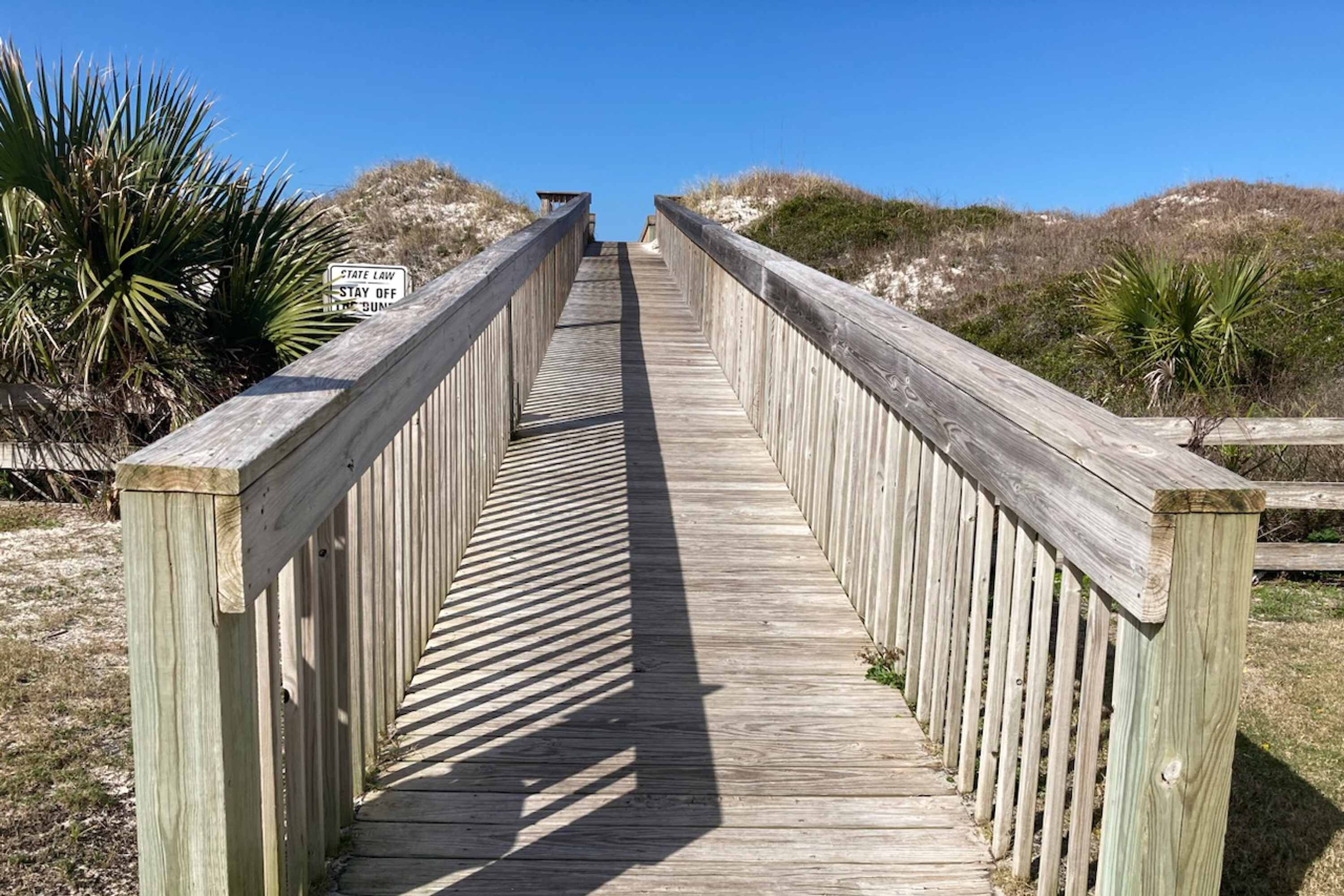 A wooden boardwalk leading to a beach with a 'Stay Off the Dump' sign.