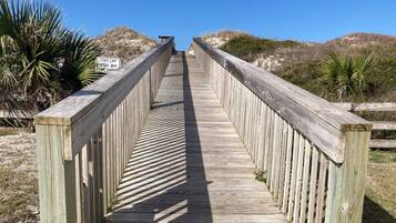 A wooden boardwalk leading to a beach with a 'Stay Off the Dump' sign.