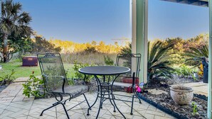 Um pátio com uma mesa redonda e duas cadeiras, rodeado por um jardim com diversas plantas e um vaso grande.