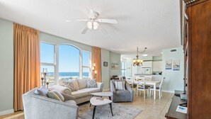 Ein geräumiges Wohnzimmer mit großem Fenster, Deckenventilator und Essbereich mit Tisch und Stühlen.