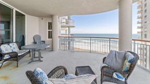 Ein Balkon mit Korbmöbeln, einem Tisch und Blick auf den Strand.