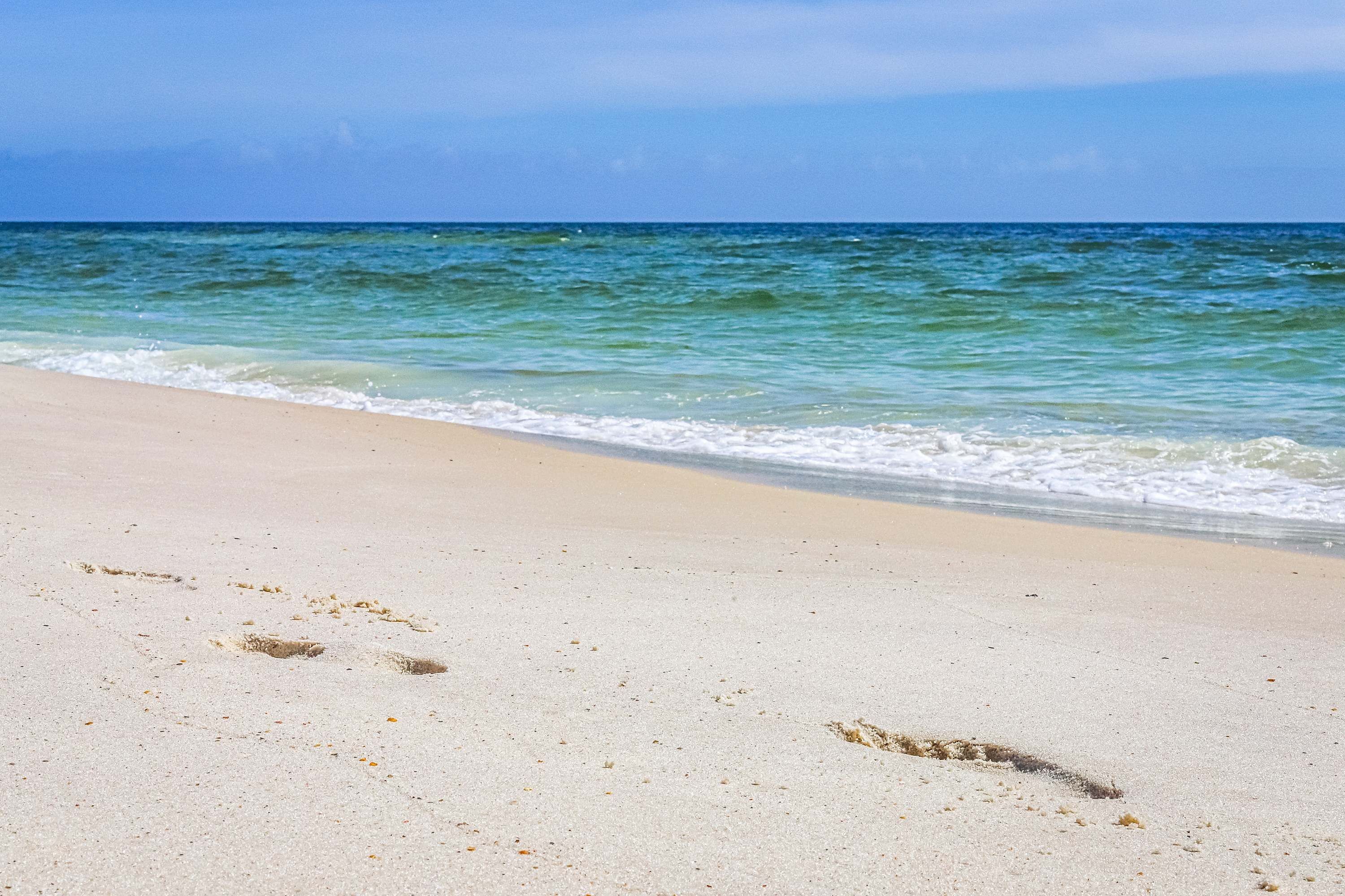 A beach with footprints in the sand and a clear view of the ocean.