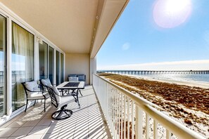 Ein Balkon mit Tisch und Stühlen mit Blick auf einen Strand und einen Steg.