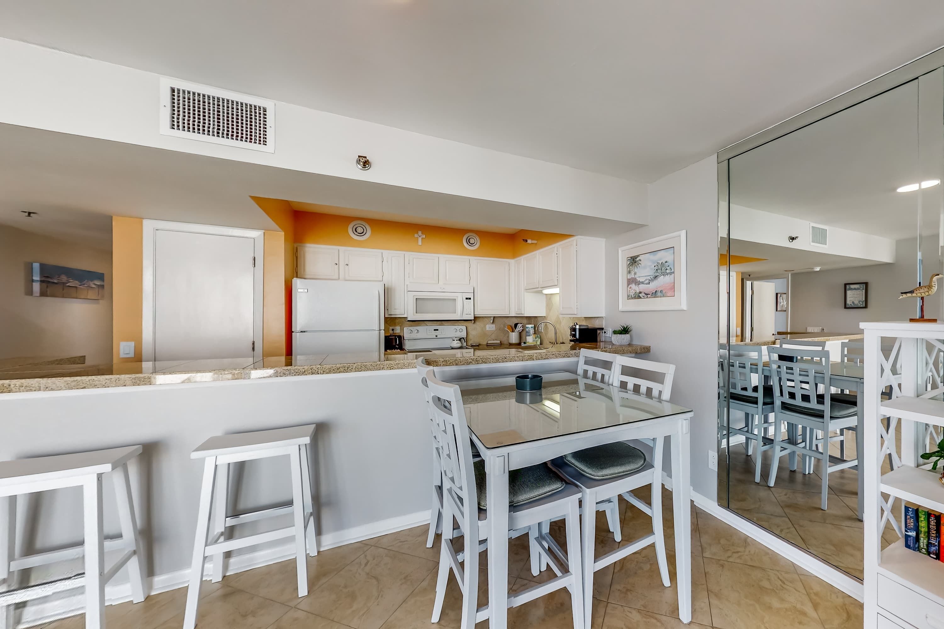 A modern kitchen with white cabinets, a central island with seating, and a dining area with chairs and a table.