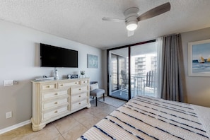 A bedroom with a large bed, a dresser, a flat-screen TV, a ceiling fan, and a sliding glass door leading to a balcony. - Gulf view condo with WiFi, AC, balcony, on-site pool, hot tub, & beach access (Miramar Beach)