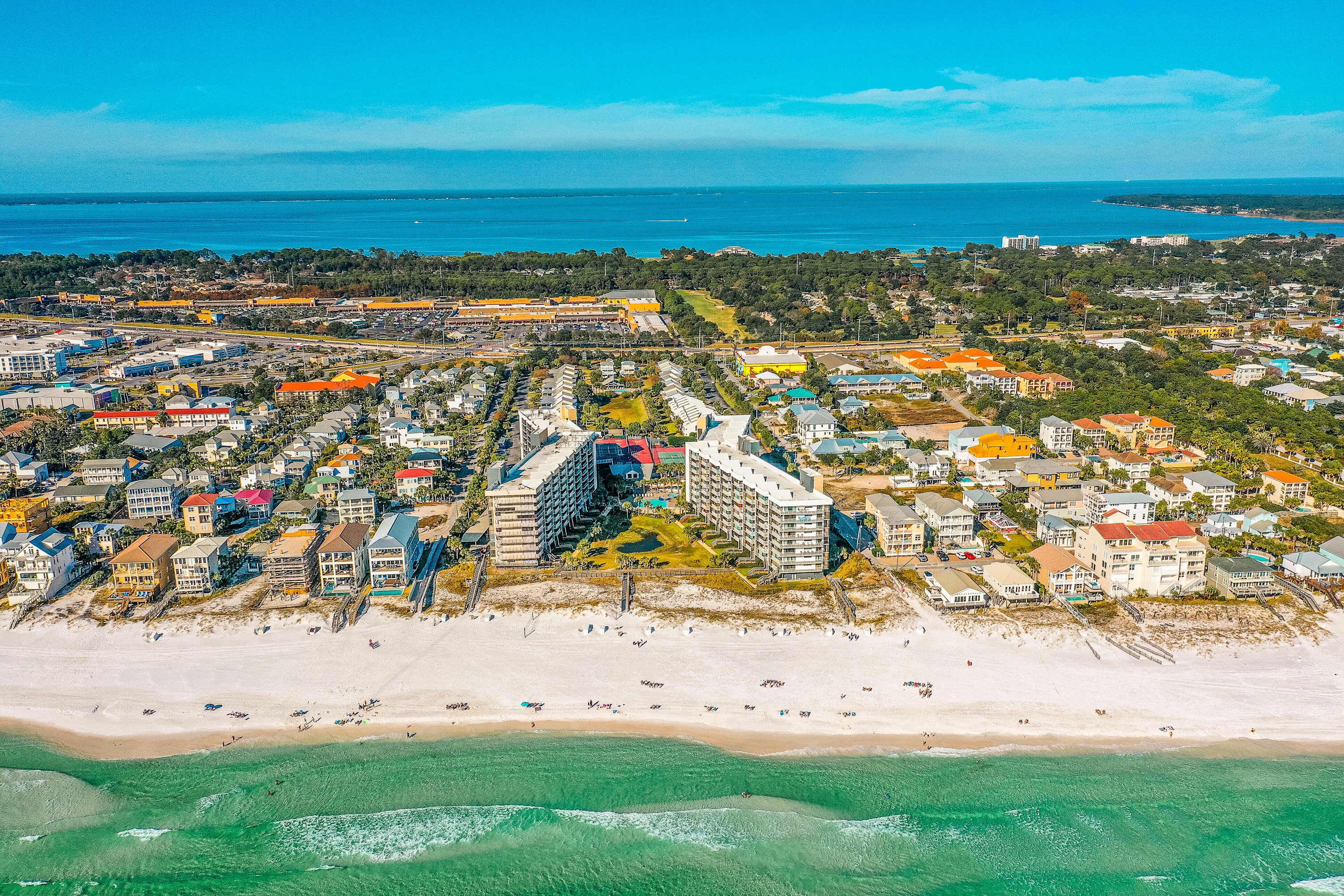 Vista aérea de un pueblo costero con playa, edificios residenciales y un gran complejo hotelero.