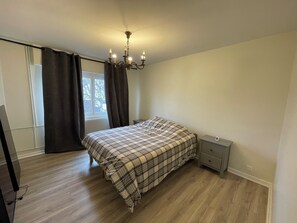 Un dormitorio con cama, mesita de noche, cómoda, ventana con cortinas y candelabro.