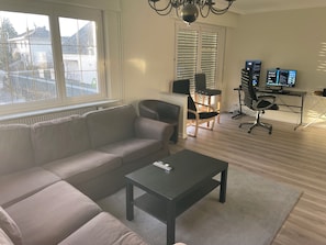 Una sala de estar moderna con un sofá, una mesa de centro y un escritorio con dos monitores.