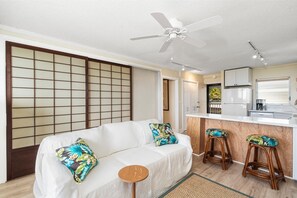 A modern living room with a sofa, two matching armchairs, a small wooden table, and a kitchen area with a counter and stools. - Kailua Village#604 High Floor, Gorgeous Remodeled 1 bedroom, in Heart of Town (Kailua Kona)