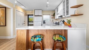 Una cocina moderna con armarios blancos, encimera de mármol y taburetes de madera con tapicería floral.