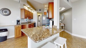 A kitchen with granite countertops, wooden cabinets, a stainless steel refrigerator, and a coffee maker. - Surfside Resort  1211 (3) (Miramar Beach)