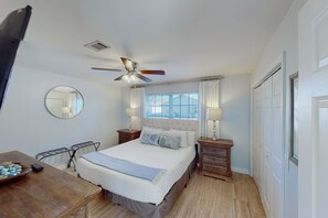 A bedroom with a bed, bedside tables, a ceiling fan, a window with curtains, a mirror, and a wooden floor. - Dog-friendly townhouse near the beach with outdoor pool, water views, & AC (Miramar Beach)