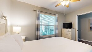 Une chambre d’hôtel avec un lit, un ventilateur de plafond, une télévision, une commode et une fenêtre avec des stores.