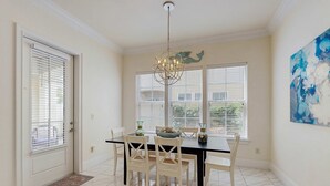 A dining area with a black table, white chairs, a chandelier, and a large window with blinds.