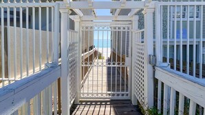A gated pathway leading to a beach, flanked by white railings and a wooden deck.