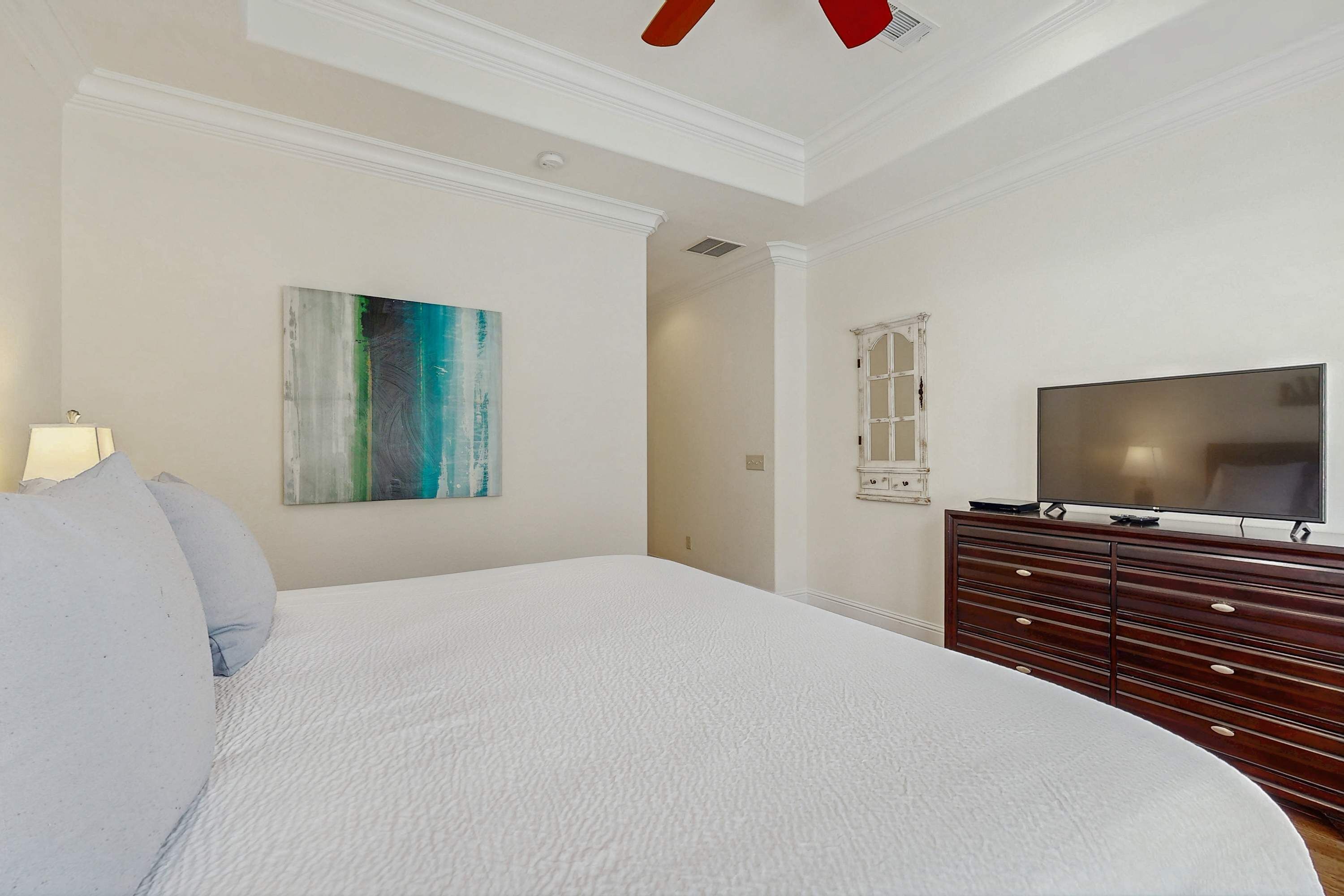 Un dormitorio con una cama grande, un aparador, un televisor y un cuadro en la pared.