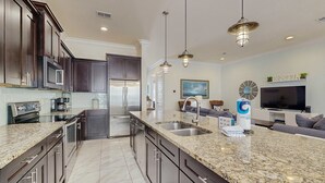 A modern kitchen with dark wood cabinets, granite countertops, stainless steel appliances, and pendant lighting.