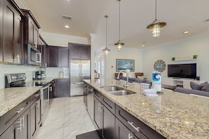 A modern kitchen with dark wood cabinets, granite countertops, stainless steel appliances, and pendant lighting. - Townhouse with private patio, pool & private beach access - snowbirds welcome (Miramar Beach)