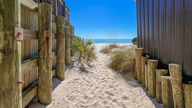 A sandy pathway flanked by wooden structures leading to a beach.