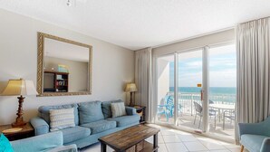 Ein Wohnzimmer mit Sofa, Couchtisch und einem großen Spiegel. Ein Balkon bietet Blick auf den Ozean.