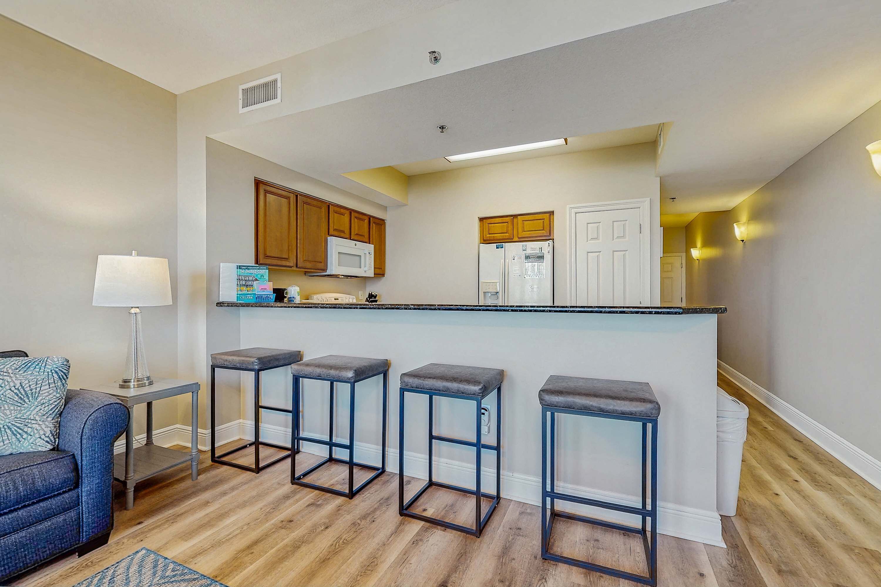 A modern kitchen with wooden cabinets, a white refrigerator, and a bar area with stools.