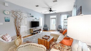 Uma sala de estar com televisão, sofá, cadeiras e um vaso decorativo.