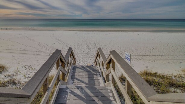 A wooden staircase leading to a beach with a sign indicating a boardwalk. - Spacious condo with bay views, renovated pool, hot tub, & beach access! (Miramar Beach)