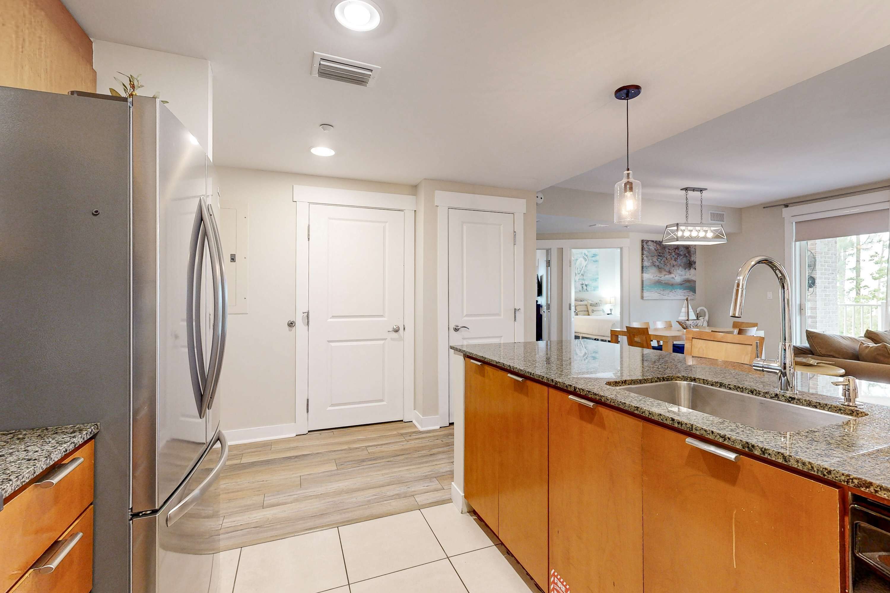 A modern kitchen with a stainless steel refrigerator, wooden cabinets, a granite countertop, and a built-in sink.