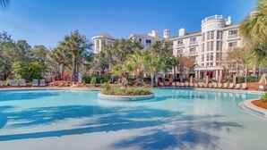 A large pool with a circular island, surrounded by palm trees and lounge chairs. - Spacious condo with bay views, renovated pool, hot tub, & beach access! (Miramar Beach)