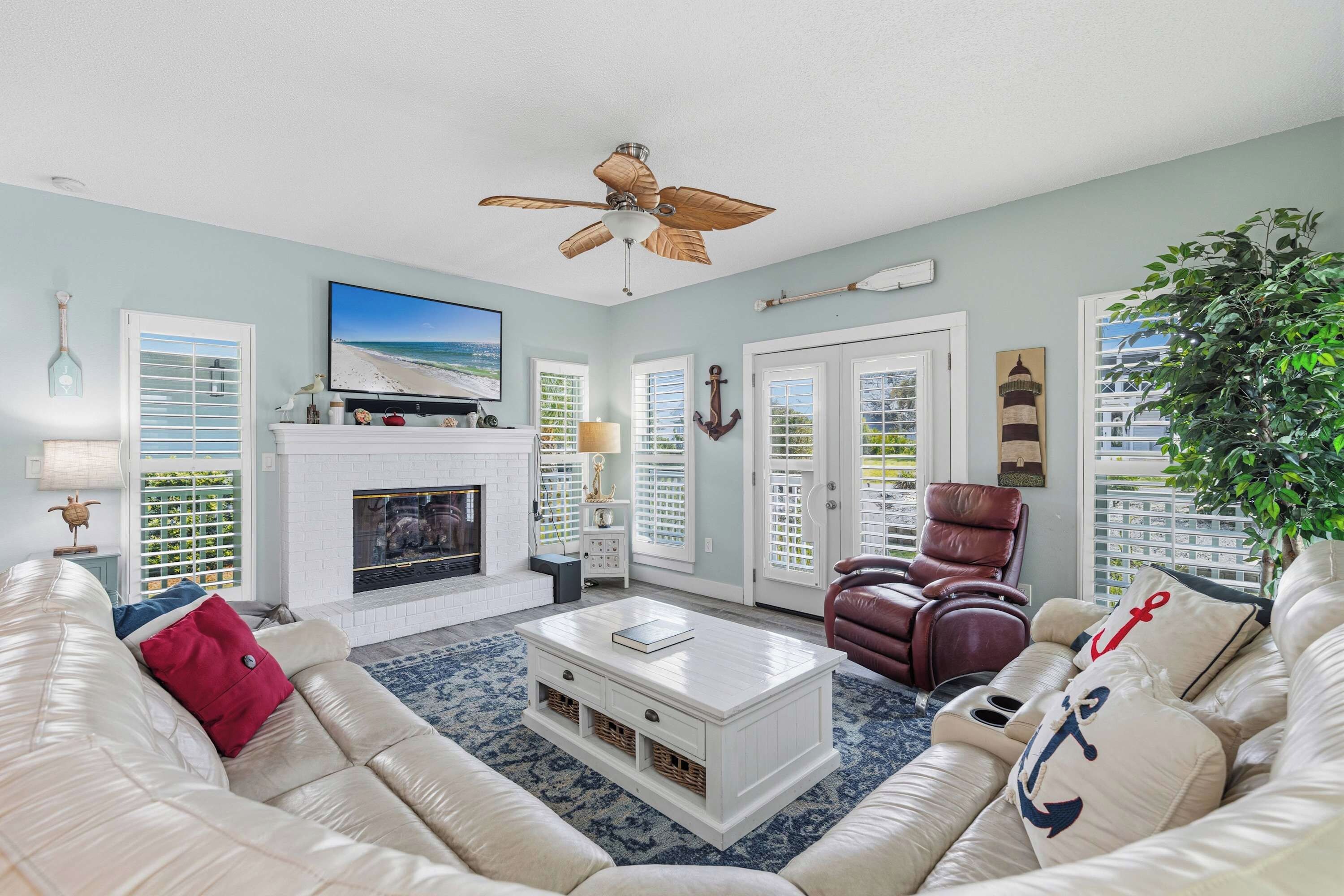A living room with a fireplace, white furniture, a ceiling fan, and nautical decor.