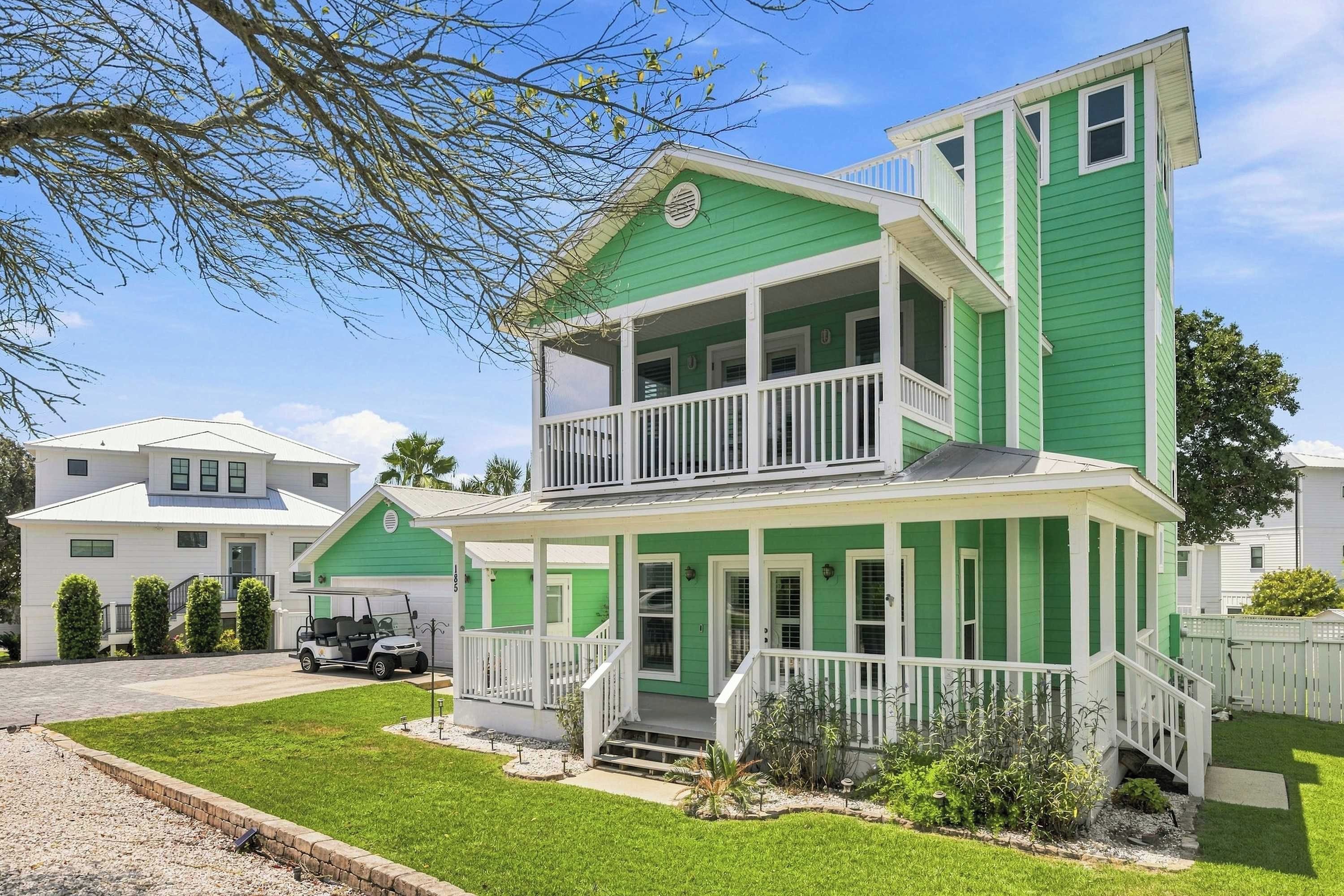 A two-story house with a green exterior, a balcony on the upper floor, and a front porch.