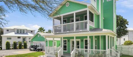 Une maison à deux étages, avec une façade verte, un balcon à l’étage supérieur et un porche à l’avant.