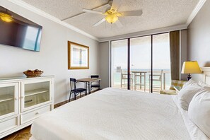A hotel room with a large bed, a desk with two chairs, a television, a ceiling fan, and a view of the ocean. - Gulf-front studio with gorgeous views, shared pool & hot tub, central AC, WiFi (Miramar Beach)