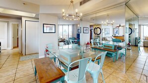 Un vaste espace dédié à la salle à manger, avec une table à plateau en verre, des chaises bleu clair et un lustre.