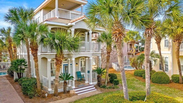 Une maison à deux étages dotée d’un balcon, entourée de palmiers et d’une pelouse bien entretenue.