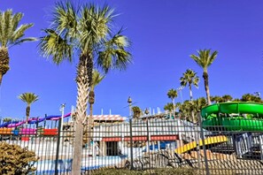 A fenced area with palm trees, a water slide, and a building with a red and white striped awning. - Charming home with wraparound balcony & central AC - 1/2 block to the beach (Miramar Beach)