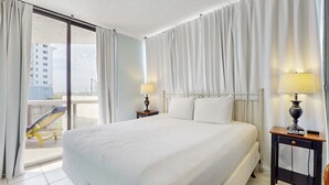 Ein Hotelzimmer mit einem großen Bett, zwei Nachttischen mit Lampen, einem Balkon mit einem Stuhl und Blick auf Gebäude.