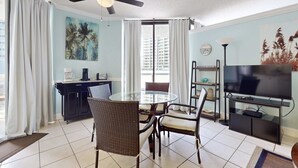 Ein modernes Wohnzimmer mit einem runden Glastisch, Korbstühlen, einem Deckenventilator, einem Flachbildfernseher und Kunstwerken an den Wänden.