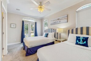 Une chambre d’hôtel avec deux lits, un ventilateur de plafond, une fenêtre avec des stores, une table de chevet avec une lampe et un tableau au mur.