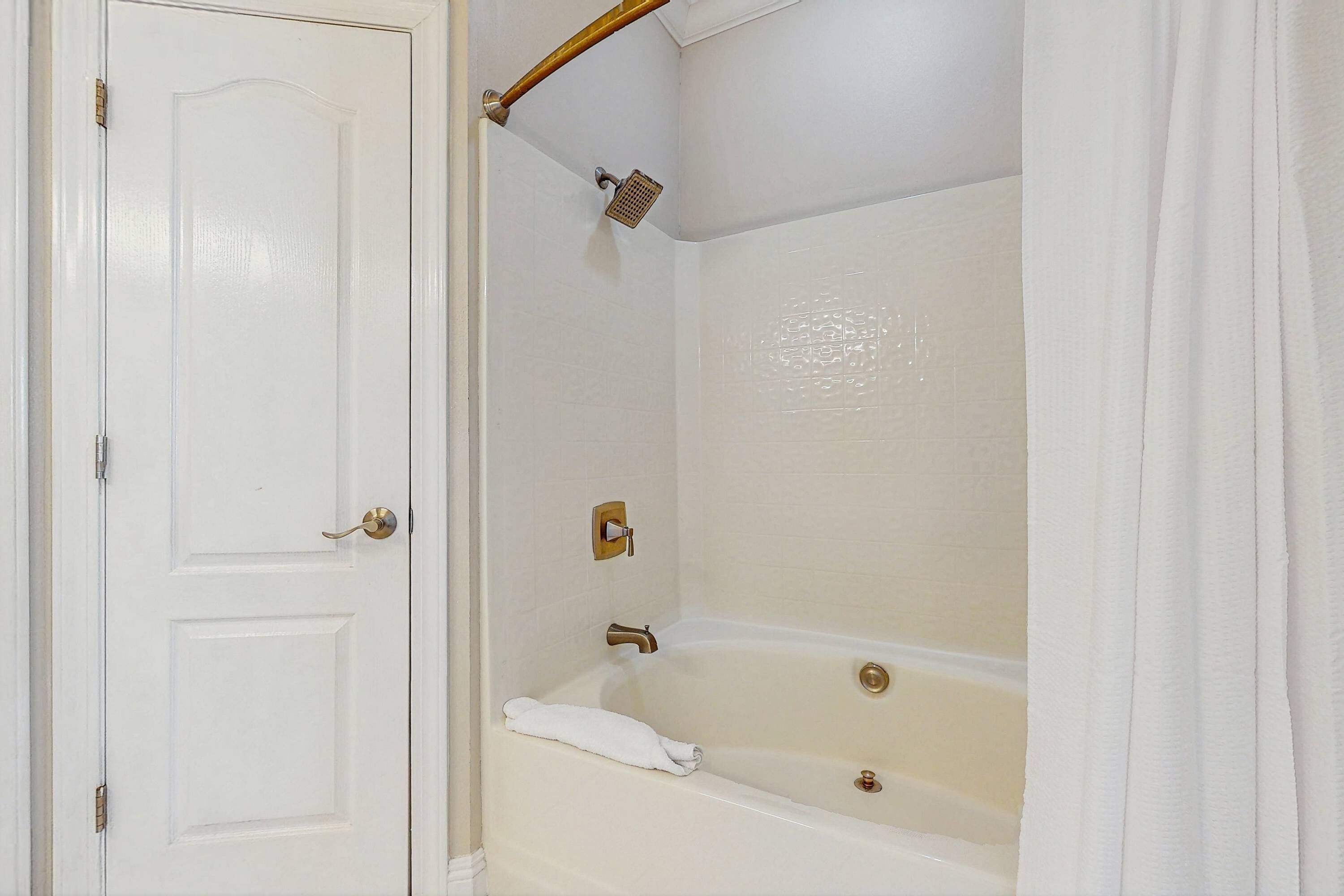 A bathroom with a white door, a bathtub, and a showerhead.