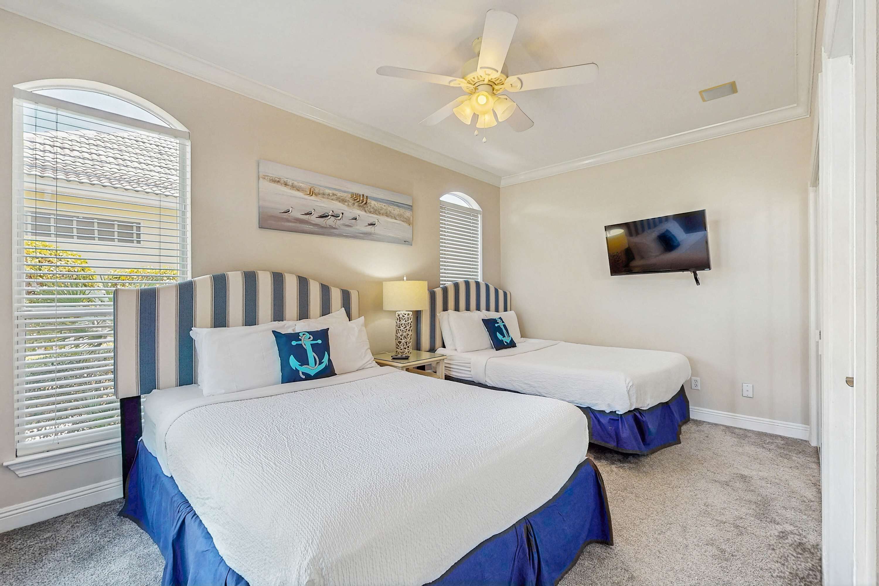 A hotel room with two beds, a ceiling fan, a TV, and a window with blinds.