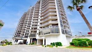 A high-rise hotel with multiple balconies, a covered entrance, and a palm tree nearby. - Cheerful 10th Floor Condo with Shared Pool & Hot Tub, WiFi, and Central AC (Miramar Beach)
