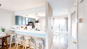 A modern kitchen with a central island, bar stools, and a dining area with white chairs. - Beautifully updated 2nd-floor condo near the beach with pool, balcony, W/D, & AC (Miramar Beach)