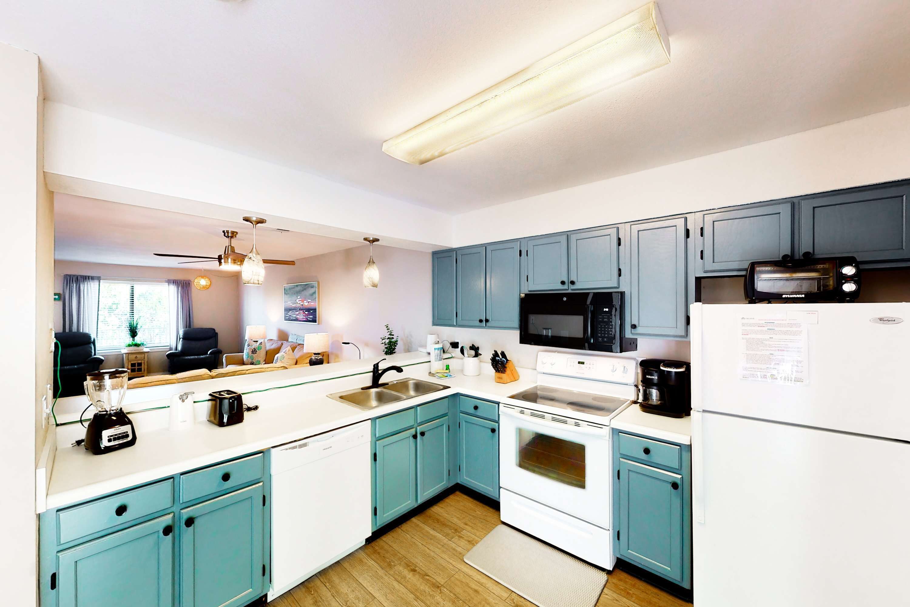 A modern kitchen with teal cabinets, white appliances, and a wooden floor.