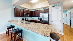 A modern kitchen with dark wood cabinets, a granite countertop, stainless steel appliances, and a bar area with stools. - Beach service included at gated coastal condo with pool, hot tub, W&D, & balcony (Miramar Beach)