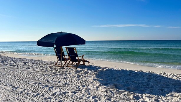 A beach with two wooden chairs and a blue umbrella. - Beach service included at gated coastal condo with pool, hot tub, W&D, & balcony (Miramar Beach)