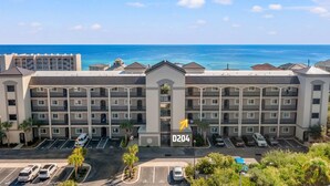 A multi-story hotel with a central atrium, parking lot, and a view of the ocean. - Beach service included at gated coastal condo with pool, hot tub, W&D, & balcony (Miramar Beach)