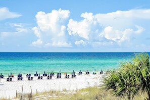A beach with rows of sun loungers and umbrellas, a clear blue sky, and calm turquoise waters. - Sunlit condo with washer&dryer, AC, pool, outdoor hot tub, & beach access (Miramar Beach)